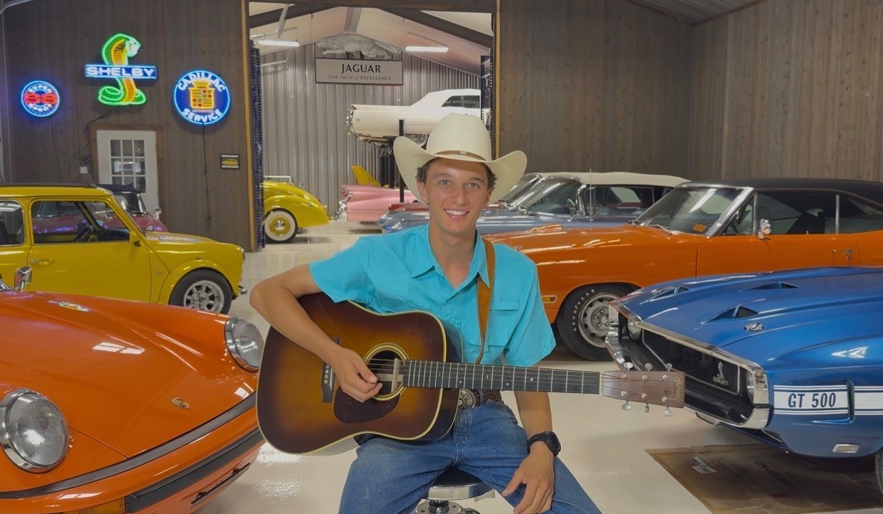 Matthew Underwood smiling with his acoustic guitar in the garage